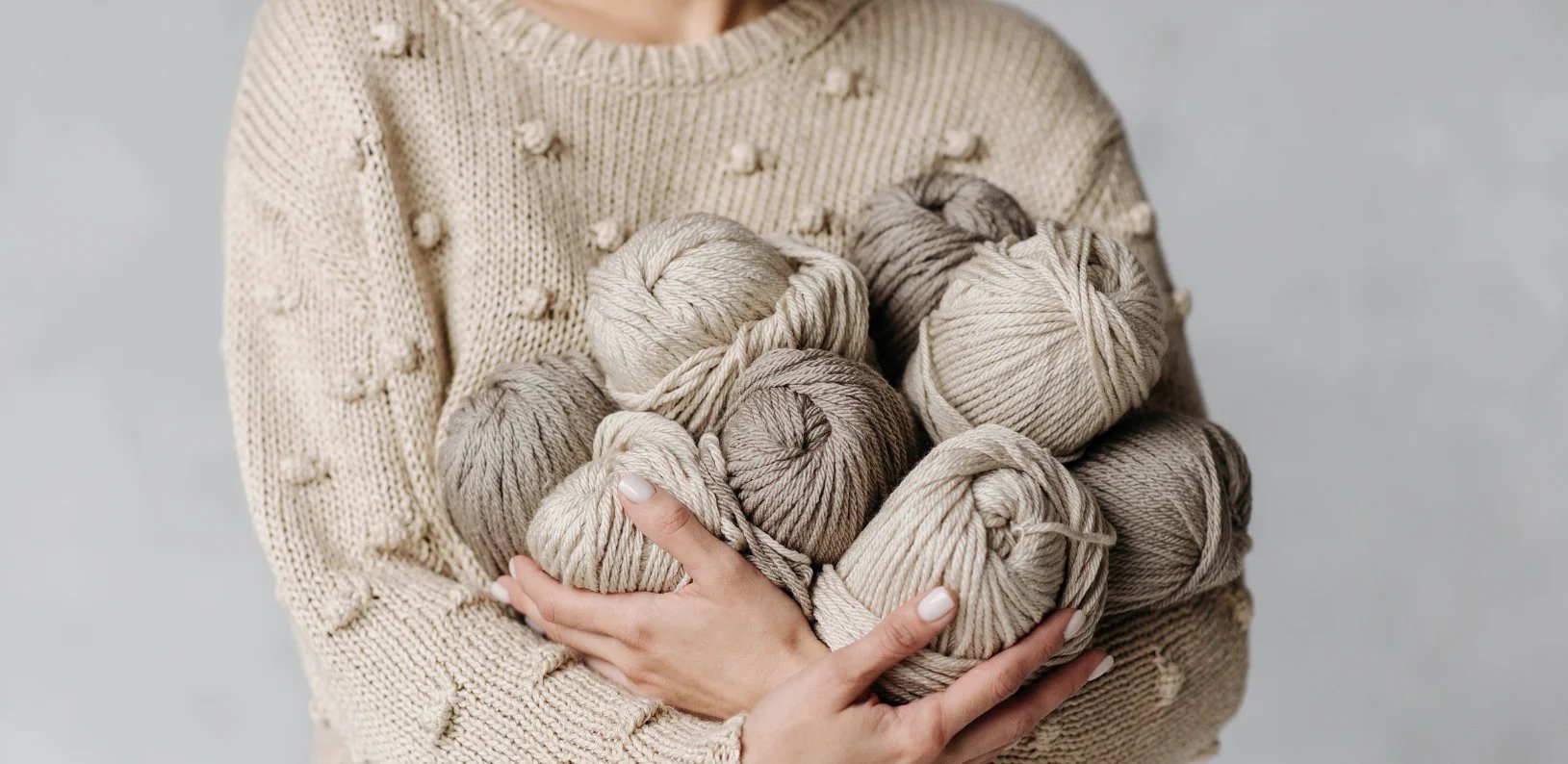 Na imagem, uma mulher segurando vários rolos de linha de crochê para fazer artesanato